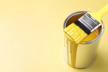 Can of paint and brush on yellow background, closeup. Space for text