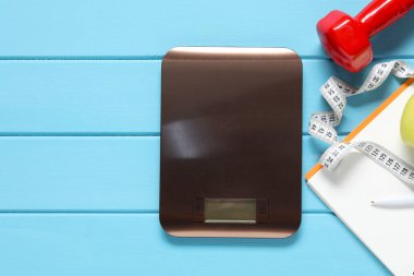 Elektronik mutfak ölçeği, mezura ve açık mavi ahşap masa üzerinde dambıl, düz zemin. Metin için boşluk