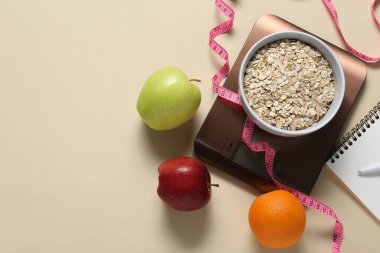 Elektronik mutfak ölçeği, mezura, not defteri ve bej masadaki ürünler, düz konum. Metin için boşluk