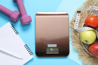 Elektronik mutfak ölçeği, mezura, dambıl, not defteri ve açık mavi arka plandaki ürünler, düz yatak. Kalori kontrolü
