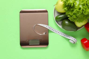 Elektronik mutfak ölçeği, mezura, açık yeşil zemin üzerinde dambıl ve ürünler, düz zemin. Diyet