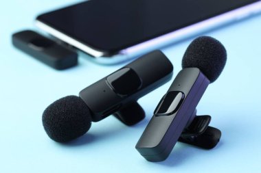 Açık mavi arkaplanda kablosuz alıcısı olan Lavalier mikrofonlar ve akıllı telefon.