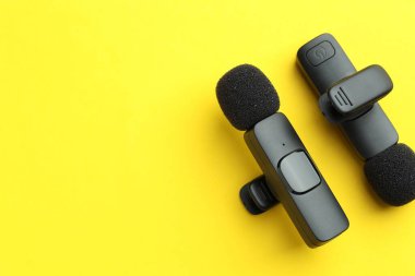 Lavalier mikrofonlar sarı arka planda, düz yerde. Metin için boşluk