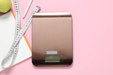 Elektronik mutfak ölçeği, mezura, pembe arka planda defter ve kalem, düz konum. Metin için boşluk