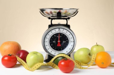 Ürünlerle birlikte mekanik mutfak terazisi ve bej arka planda beyaz ahşap masadaki şerit. Diyet