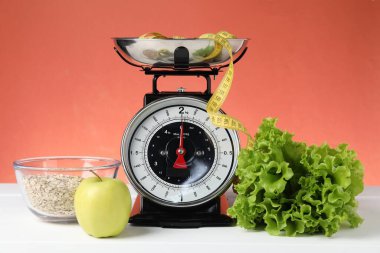 Ürünlerle birlikte mekanik mutfak terazisi ve mercan zeminine karşı beyaz ahşap masadaki şerit. Diyet