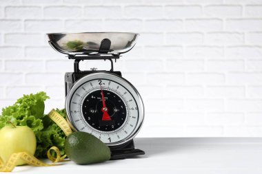 Mutfak terazisinde bir kase ürün ve tuğla duvara dayalı beyaz ahşap masada şerit var. Metin için boşluk