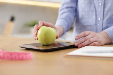 Mutfak terazisinde elmayı tartan kadın, kapalı masa, yakın plan.