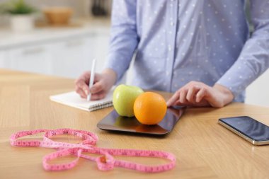 Tahta masada meyveleri tartan ve not defterine yazan kadın, yakın plan.