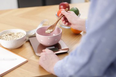 Mutfak terazisinde yulaf ezmesi tartan kadın ahşap masada, yakın plan.