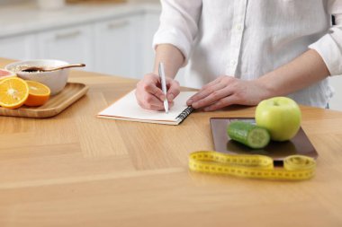 Ürünleri tartan ve not defterine yazan kadın. Tahta masada, yakın plan.