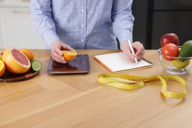 Turuncu ağırlıklı kadın, ahşap masada deftere yazı yazıyor, yakın plan.