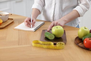 Ürünleri tartan ve not defterine yazan kadın. Tahta masada, yakın plan.