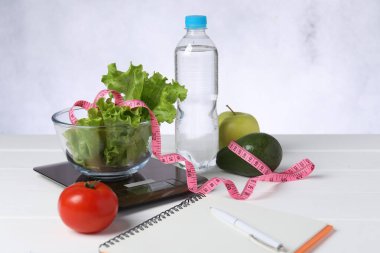 Mutfak pulları, ürünler, su, defter ve mezura beyaz ahşap masa üzerinde.