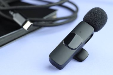 Açık mavi zemin üzerinde Lavalier mikrofon, kablo ve defter, yakın plan