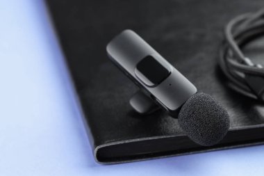 Açık mavi zemin üzerinde Lavalier mikrofon, kablo ve defter, yakın plan