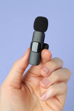 Açık mavi arka planda lavalier mikrofon tutan kadın, yakın plan.