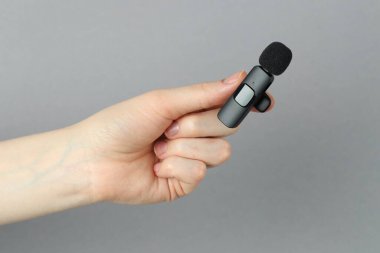 Açık gri arkaplanda lavalier mikrofon tutan kadın, yakın plan.