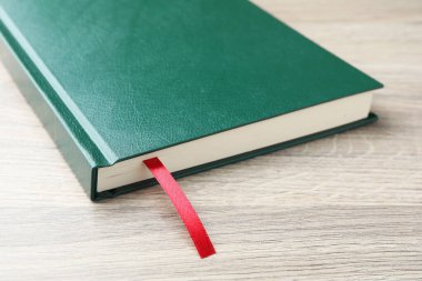Açık ahşap masa üzerinde kırmızı kurdele yer imi olan kitap, yakın plan.