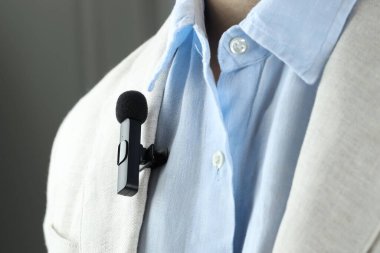 Gri arka planda takım elbisesine mikrofon takmış bir adam, yakın plan.