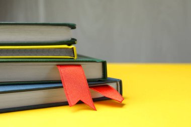 Sarı masa üzerinde kırmızı kurdele yer imleri olan kitaplar gri arka planda, yakın plan. Metin için boşluk