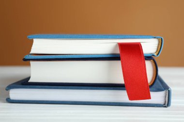 Kırmızı kurdele kitap ayracı ve mavi olanlar beyaz ahşap masa üzerinde kahverengi arkaplan, yakın plan