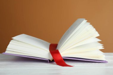 Kahverengi arkaplana karşı beyaz ahşap masa üzerinde kırmızı kurdele yer imi olan kitabı aç, kapat