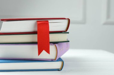 Kırmızı kurdele ayıracı ve gri duvara karşı beyaz ahşap masa üzerinde renkli kitap, yakın plan. Metin için boşluk