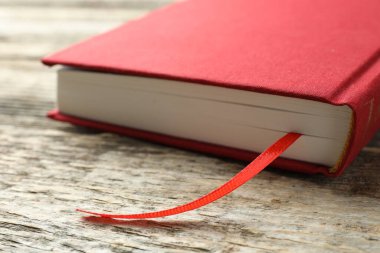 Ahşap masada kırmızı kurdele yer imi olan bir kitap, yakın plan.