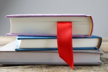 Kırmızı kurdele yer imi ve ahşap masadaki renkli kitap gri arkaplanda, yakın plan
