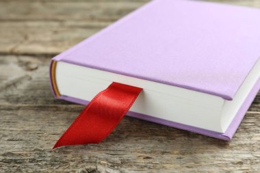Ahşap masada kırmızı kurdele yer imi olan bir kitap, yakın plan.