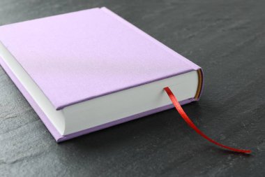 Koyu desenli masa üzerinde kırmızı kurdele yer imi olan kitap, yakın plan.