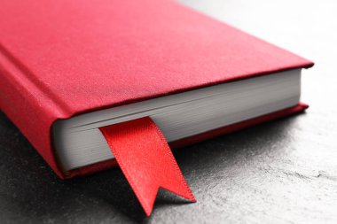 Koyu desenli masa üzerinde kırmızı kurdele yer imi olan kitap, yakın plan.