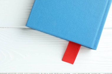 Beyaz ahşap masa üzerinde kırmızı kurdele yer imi olan kitap, üst görünüm