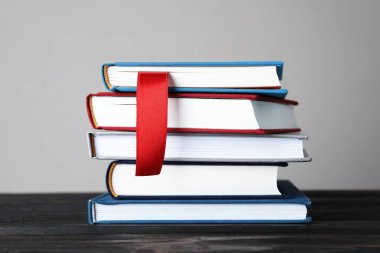 Kırmızı kurdele yer imi ve ahşap masadaki renkli kitap gri arkaplanda, yakın plan