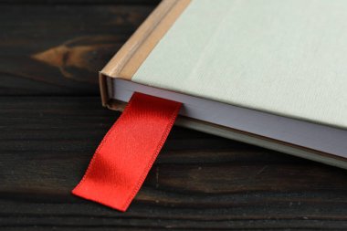 Ahşap masada kırmızı kurdele yer imi olan bir kitap, yakın plan.