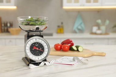 Mutfak pulları yeşillik, mezura, defter ve sebzeler açık mermer masa içinde.