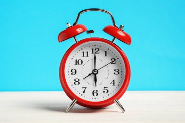 Beyaz ahşap masada açık mavi zemin üzerinde bir kırmızı alarm saati