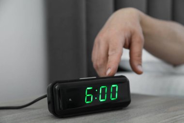 Kapalı bir odada, komodinin üzerindeki dijital çalar saati kapatan adam.