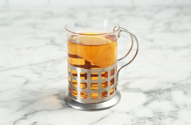 Beyaz mermer masanın üzerinde metal tutacağında cam çay fincanı, yakın plan.