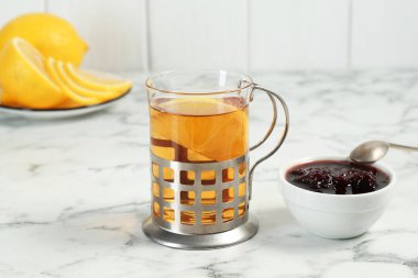 Metal tutacakta bir bardak çay, reçel ve limon dilimleri beyaz mermer masada, yakın plan.
