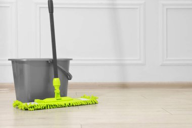 Beyaz duvarın yanındaki tahta zeminde mikrofiber paspas ve kova. Metin için boşluk