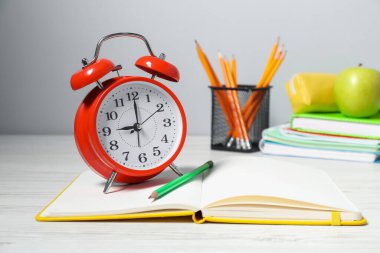 Alarm saati, kırtasiye malzemesi ve beyaz ahşap masada elma. Bilgi zamanı