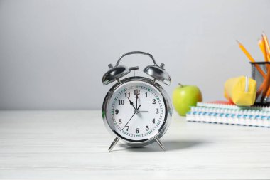 Alarm saati, kırtasiye malzemesi ve beyaz ahşap masada elma. Bilgi zamanı