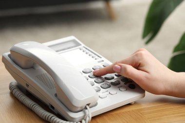 Kadın ahşap masadaki telefon numarasını bulanık arkaplana karşı çeviriyor.