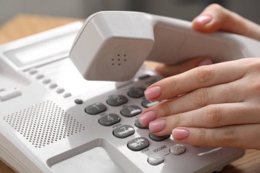 Kadın ahşap masadaki telefon numarasını bulanık arkaplana karşı çeviriyor.