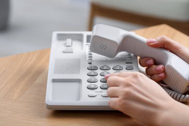 Kadın ahşap masadaki telefon numarasını bulanık arkaplana karşı çeviriyor.