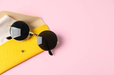 Şık güneş gözlüklü ve açık pembe arka planda temizlik bezli çanta, üst manzara. Metin için boşluk