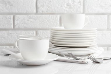 Different clean dishware on white table near brick wall