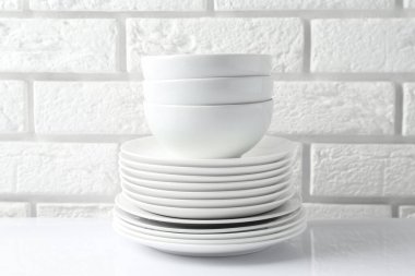 Different clean dishware on white table near brick wall